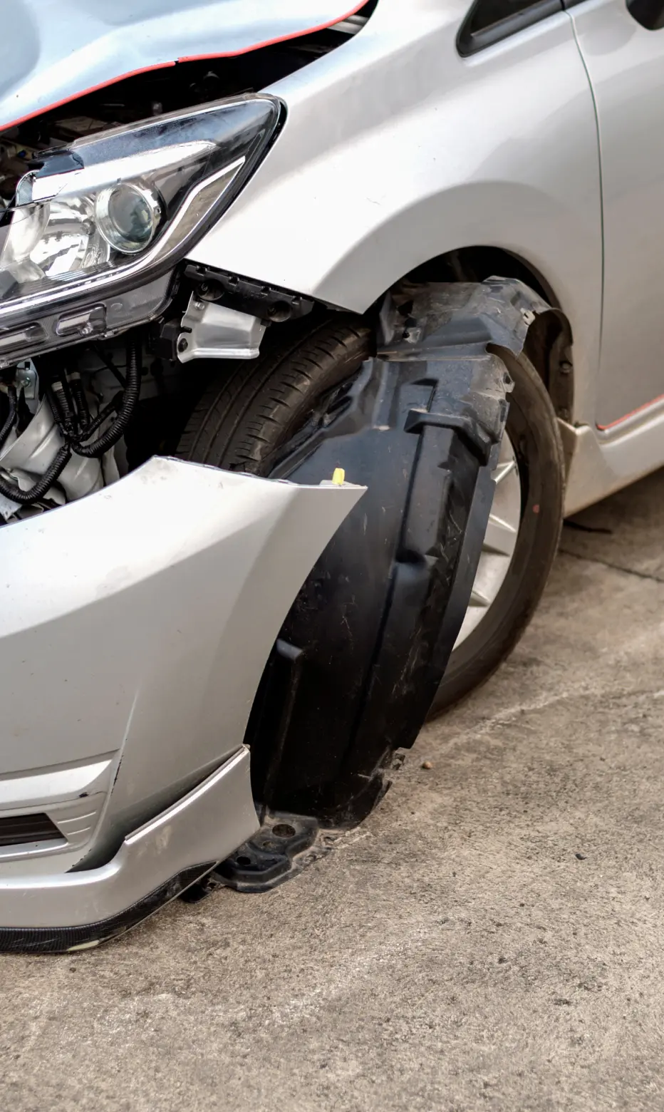 Close-up of a silver car with significant front-end damage, including a crumpled hood and exposed wheel, indicating a recent collision. Emphasizes accident impact.