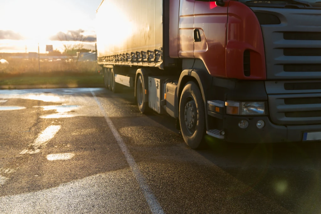 A red semi-truck parked on a wet road during sunset, with warm light reflecting off the pavement, creating a serene and calm atmosphere.