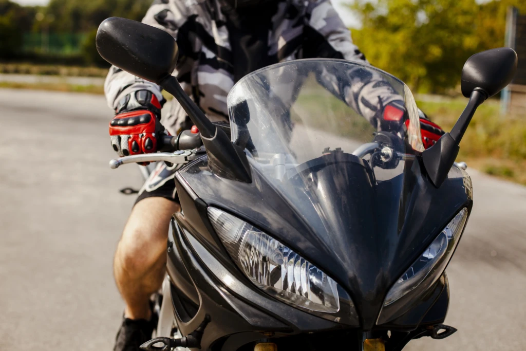 Person riding a sleek black motorcycle on a sunny day. They wear a camo jacket and red gloves, exuding a sense of adventure and freedom.