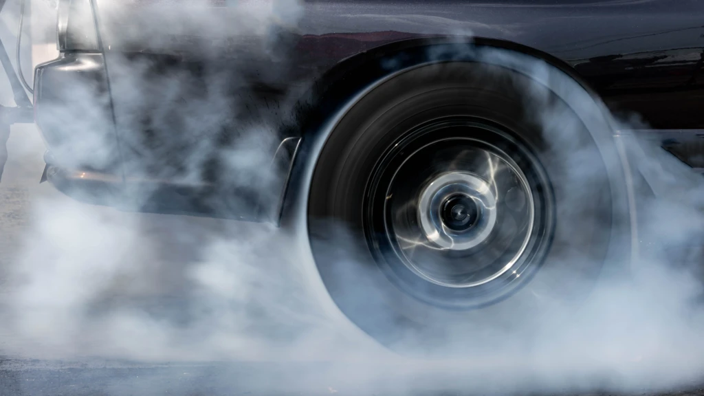 A spinning car wheel surrounded by thick smoke, indicating a burnout. The smoky atmosphere suggests speed, power, and intensity.