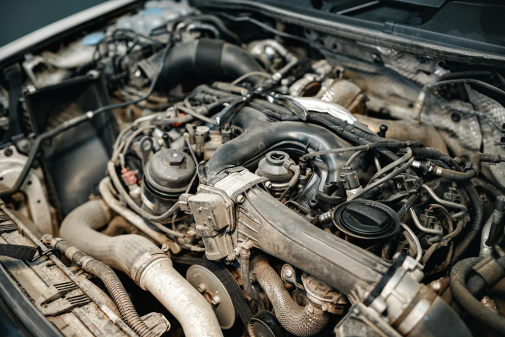 Close-up of a car engine, showing complex intertwining pipes, wires, and metal components. The image conveys a sense of mechanical intricacy.